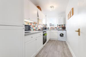 a kitchen with white cabinets and a washer and dryer at The Cooperage - 2 Bedroom, 2 Bathroom with Garden in Crail