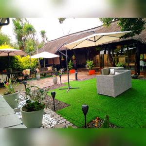 a patio with a lawn with chairs and umbrellas at Pari Guest House in Middelburg