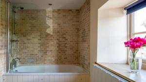 une salle de bain avec une baignoire et un vase de fleurs roses dans l'établissement Hope Cottage, à Naunton