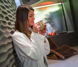 a woman drinking from a coffee cup next to a tv at Hotel Donna Lucia in Ponzano Veneto