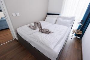 a bed with white sheets and a pile of towels on it at Villa Bauhaus Wellness Apartman 102 in Siófok