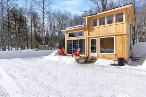 a house with two red chairs in the snow at Cozy Cabin for Intimate Wilderness Escape in Bathurst