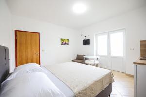 a white bedroom with a bed and a chair at Apartments Marina in Petrcane