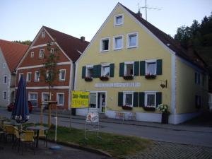 a yellow building with green shutters and tables and chairs at Pension Stauber in Hohenburg