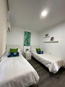 2 łóżka w pokoju z białymi ścianami i zielonymi poduszkami w obiekcie AYALA APARTAMENTO w Maladze