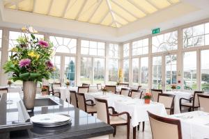 une salle à manger avec des tables blanches, des chaises et des fenêtres dans l'établissement Phyllis Court Members Club, à Henley-on-Thames