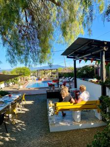 dos personas sentadas en un banco amarillo cerca de una piscina en B&B Finca Alegria de la Vida, en Pizarra