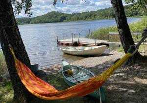 a hammock and two boats on the shore of a lake at Three Bedroom Farm Cottage Lake Access and Free Boat in Valdemarsvik