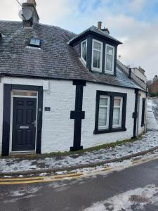 a white house with a black door on a street at Black Cat Cottage in Moffat