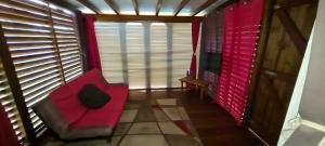 Cette chambre dispose d'une chaise rouge et d'une fenêtre avec des stores. dans l'établissement L'IXORA des îles, à Le Moule