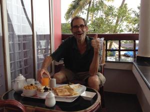 an older man giving a thumbs up while eating breakfast at Wind Surf Beach House in Alleppey