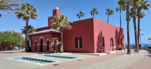 czerwony budynek z palmami przed nim w obiekcie Apartamento Estudio Ruymar Jupiter w mieście Benalmádena