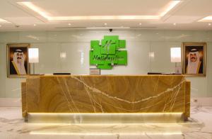 a reception desk in a lobby with a green sign on the wall at Holiday Inn Kuwait Al Thuraya City by IHG in Kuwait