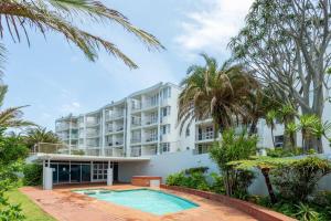 an apartment building with a swimming pool and palm trees at Ocean Pearl at Chakas Cove - Beachfront Apartment in Ballito