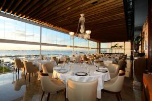 uma sala de jantar com mesas e cadeiras brancas e janelas em Cloc Marina Vista Mar p/ a Baía de Todos os Santos em Salvador