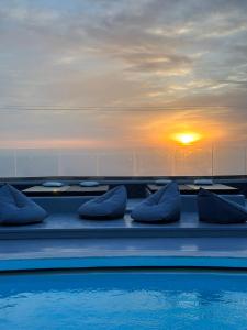 a pool with blue pillows and a sunset in the background at Abrazo Villas in Imerovigli