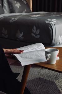 uma pessoa lendo um livro sobre uma mesa com uma xícara de café em Hotel City View Deluxe em Sarajevo