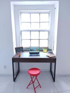 a desk with two laptops and a red stool in front of a window at São Francisco Aparts in Salvador