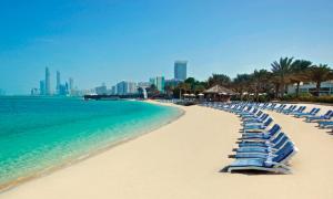 uma praia com uma fila de cadeiras e o oceano em Corniche AD - Extremely Unique Room em Abu Dhabi