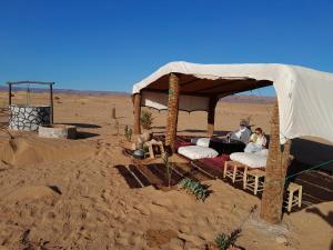dos personas sentadas bajo una tienda en el desierto en Bivouac La Dune Blanche, en Mhamid