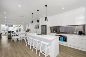 una cocina con armarios blancos y un bar con taburetes en Newly Built Spacious Beach Home, en The Entrance