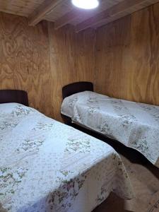 2 Betten in einem Zimmer mit Holzwänden in der Unterkunft Cabaña cerca del Aeropuerto in Puerto Montt