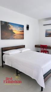 a bedroom with a white bed with a painting on the wall at Red Flamboyan Guesthouse and Restaurant in Rincon