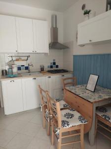 cocina con armarios blancos, mesa y sillas en Appartamento curato con giardino, en Marina Romea