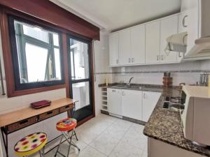 cocina con armarios blancos, ventana y 2 taburetes en P° Olmos, Panxón, bajo con jardín privado en Nigrán