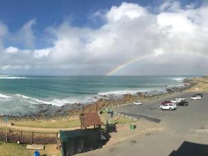 a rainbow over the ocean and a parking lot with cars at Coogee Bay Apartments in Gonubie