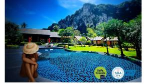 a woman in a hat sitting next to a swimming pool at Aonang Hill Krabi-SHA Extra Plus in Ao Nang Beach