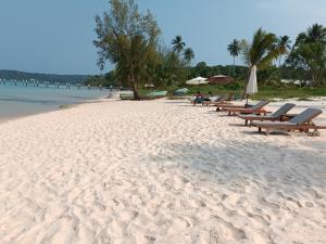 una playa de arena con bancos y sombrillas. en Luna Koh Rong en Koh Rong Island