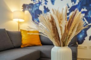 a white vase with dried grass in front of a couch at 7Seas City-Apartment Kaiserslautern - Balkon l NETFLIX l 24h Self Check-in in Kaiserslautern
