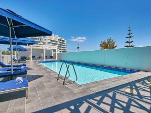 a swimming pool with two blue chairs next to a building at The Sebel Mandurah in Mandurah