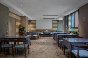 Yiwu Manting Hotel International Trade City义乌漫庭酒店 في ييوو: غرفة بطاولات وكراسي وشاشة بيضاء