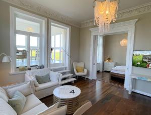 una sala de estar con muebles blancos y una lámpara de araña. en Seaside Apartments Austernbank, en Cuxhaven