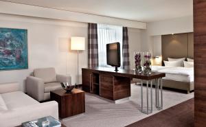a hotel room with a couch, chair, table and a television at Estrel Berlin in Berlin