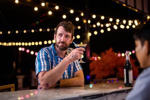 Un uomo seduto a un tavolo con un drink in mano di Confetti Garden Hotel a Vang Vieng