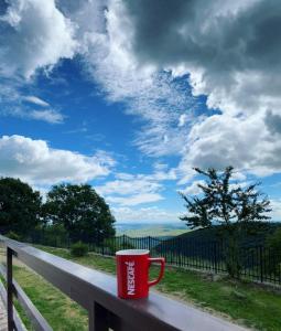 una taza de café roja sentada en una valla con un cielo en Cabana Refugiu Montan en Băişoara