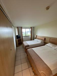 a hotel room with two beds and a window at Beach class muro alto in Porto De Galinhas