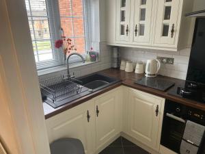 cocina con armarios blancos, fregadero y ventana en River View House St Neots - Navigation Wharf, en Saint Neots