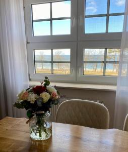 eine Vase aus Blumen auf einem Holztisch mit Fenstern in der Unterkunft Residence Black Eagle Lubmin Strand in Lubmin