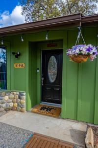 a green house with a black door and a basket of flowers at Whispering Creek Resort at Yosemite Forks in Oakhurst
