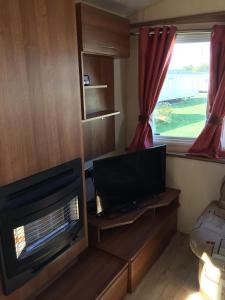 a living room with a television and a window at Beside the Seaside, Pakefield Holiday Park, Arbor Lane, Pakefield, Lowestoft NR33 7BE in Pakefield