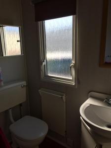 a bathroom with a toilet and a sink and a window at Beside the Seaside, Pakefield Holiday Park, Arbor Lane, Pakefield, Lowestoft NR33 7BE in Pakefield