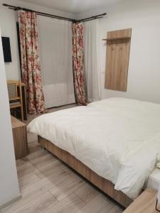 1 dormitorio con 1 cama con sábanas y cortinas blancas en Pensiunea La Nenea Iancu, en Pianu de Sus