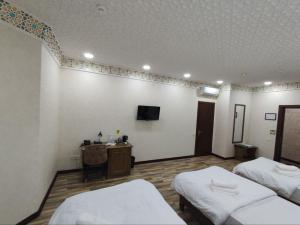 een kamer met 2 bedden, een bureau en een televisie bij Ayvan Plaza hotel in Bukhara