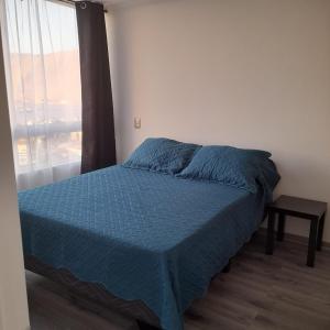 a bedroom with a bed with a blue comforter and a window at Departamento diario pleno centro vista al mar in Iquique