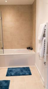 uma casa de banho com uma banheira branca e tapetes azuis em Exquisite- stylish- luxurious 2 bed apartment em The Hyde