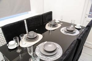 ein schwarzer Tisch mit schwarzen Stühlen, Tellern und Gläsern in der Unterkunft Newly Refurbished 3 Bedroom House close to Central London in London